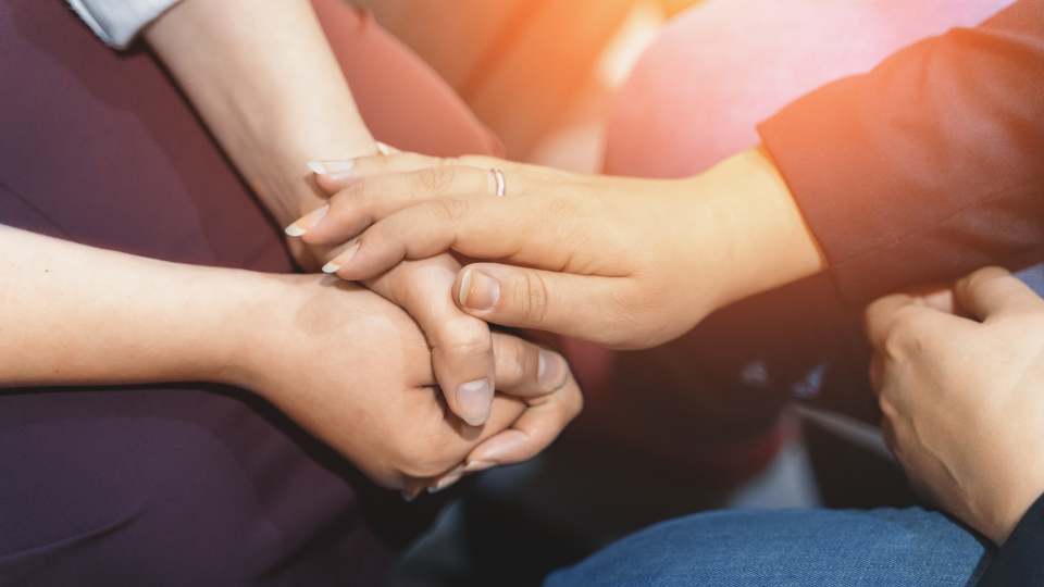 A closeup a persons hand resting on another persons clasped hands in a gesture of comfort and support