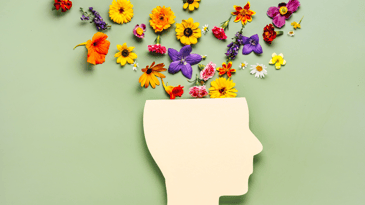 A cutout of a persons head in white construction paper with flowers coming out of the top of it against a pastel green background.