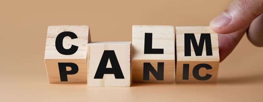 Wooden blocks with letters spelling out the word calm being shifted to spell out the word panic by someone's fingertips. 