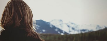 A person facing away from the camera toward snow-capped mountains to regulate anxiety. 