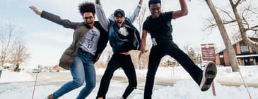 Three teenagers smiling and jumping together in celebration outdoors with snow in the background. 