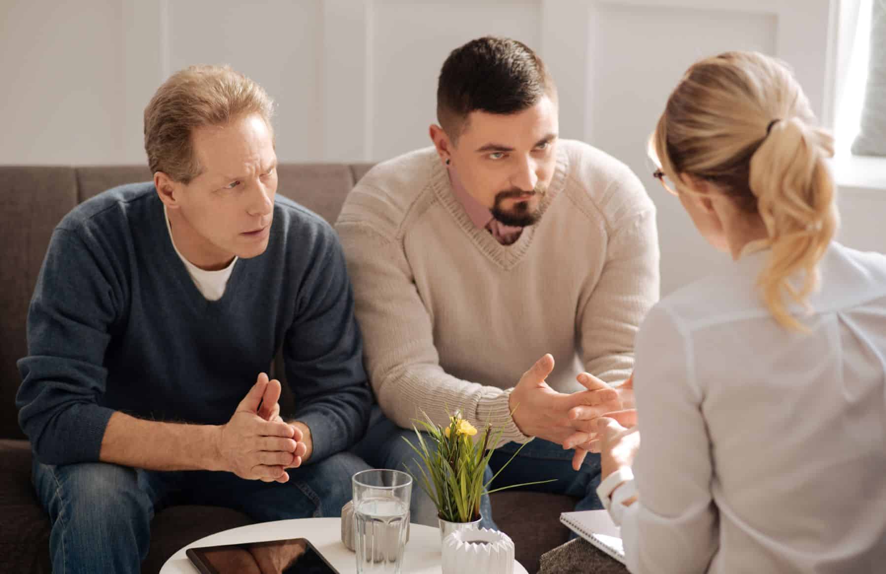 A gay couple sitting across from a therapist talking about their relationship issues.