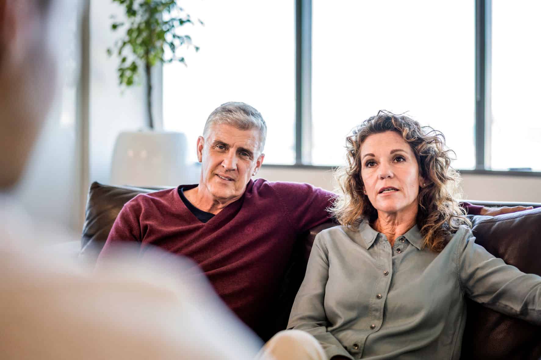 An older couple sitting on a brown couch across from a therapist to meet for marriage counseling.