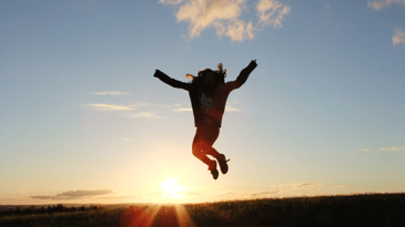 The silhouette of a person jumping with joy against a blue sky at sunset in a field