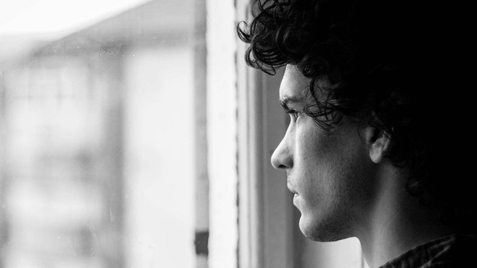 A person with dark curly hair looks out of a window.