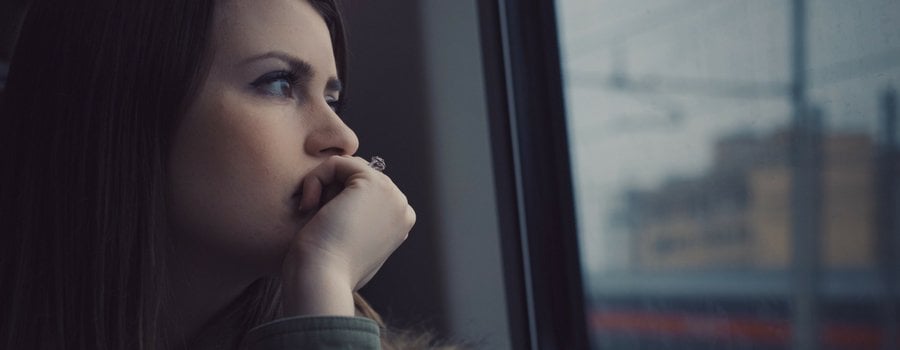 A woman staring out the window with her closed hand over her mouth with a sad expression. 