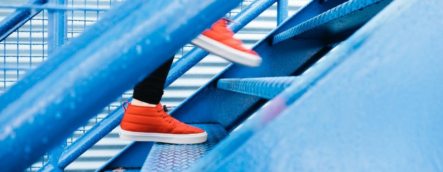 A closeup view of a bright blue outdoor staircase with a person with orange sneakers running up. 