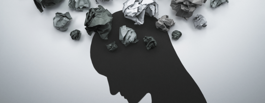 A silhouette of a person with their head down with wadded up pieces of gray paper coming out of the top of their head. 