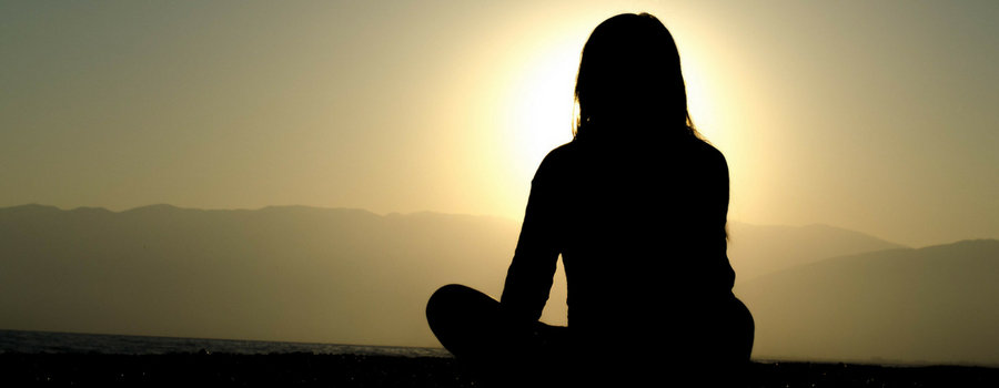 A person sitting with knees akimbo at sunset looking toward the sun. 