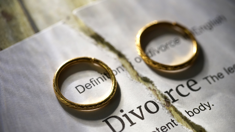 Two gold wedding bands resting on either side of a piece of paper with the word divorce typed on it with its definition. 